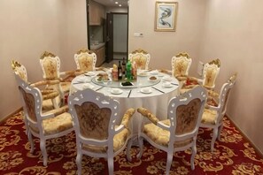 Une table de salle à manger ronde, entourée de huit chaises, recouverte d’une nappe blanche, et posée sur un sol recouvert d’un tapis rouge.