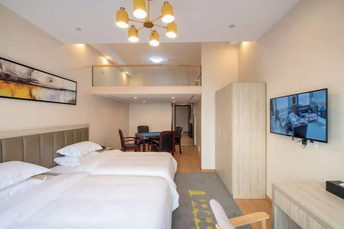 Ein Hotelzimmer mit zwei Betten, einer Essecke, einem Fernseher und einem Gemälde an der Wand.