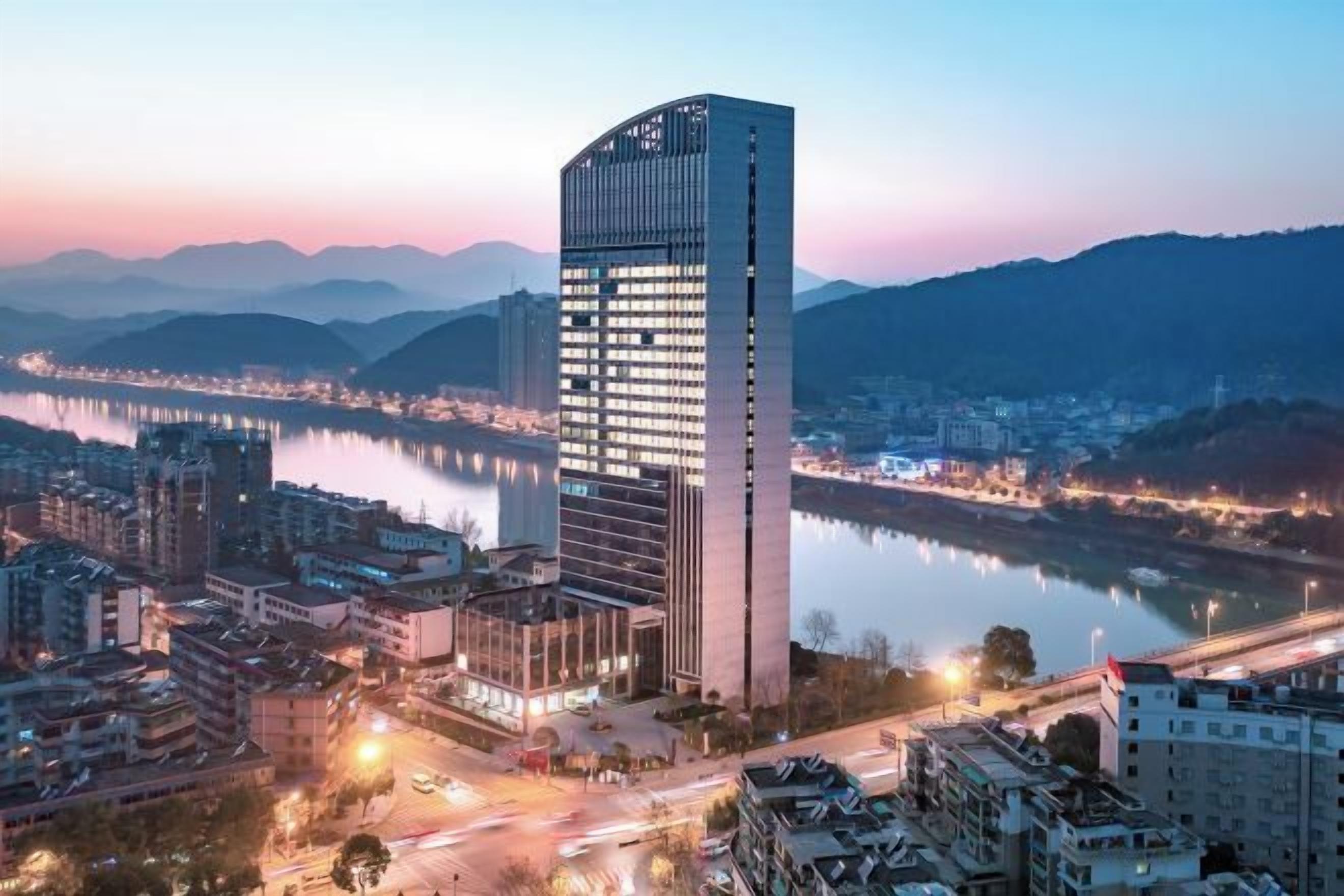 A high-rise building with a modern design, situated near a body of water and surrounded by other buildings.