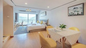 Una habitación de hotel moderna con una cama, una mesa de comedor con sillas amarillas, un cuadro en la pared y vistas al exterior.