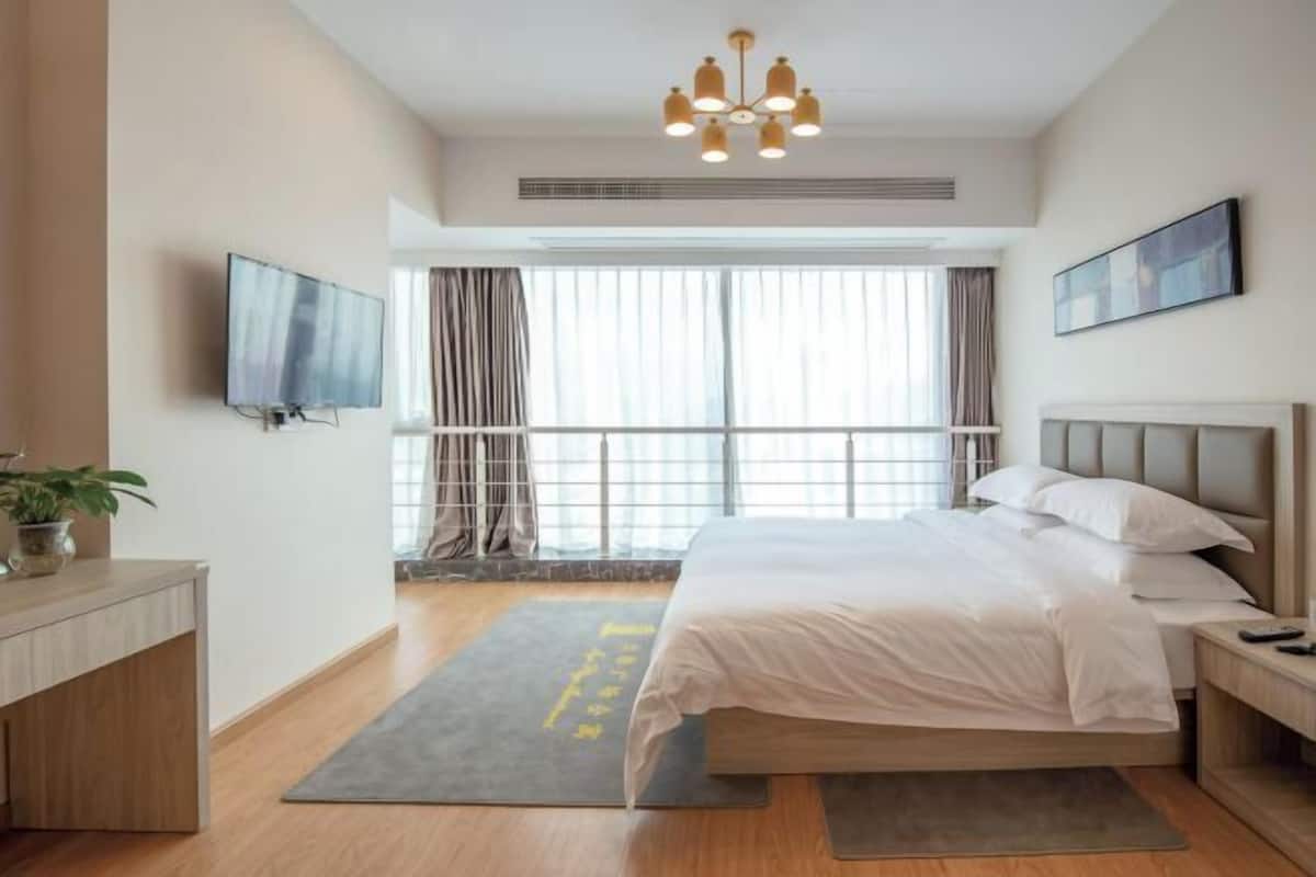 Ein modernes Hotelzimmer mit einem großen Bett, einem Fernseher, einem Schreibtisch und einem Fenster mit Vorhängen.