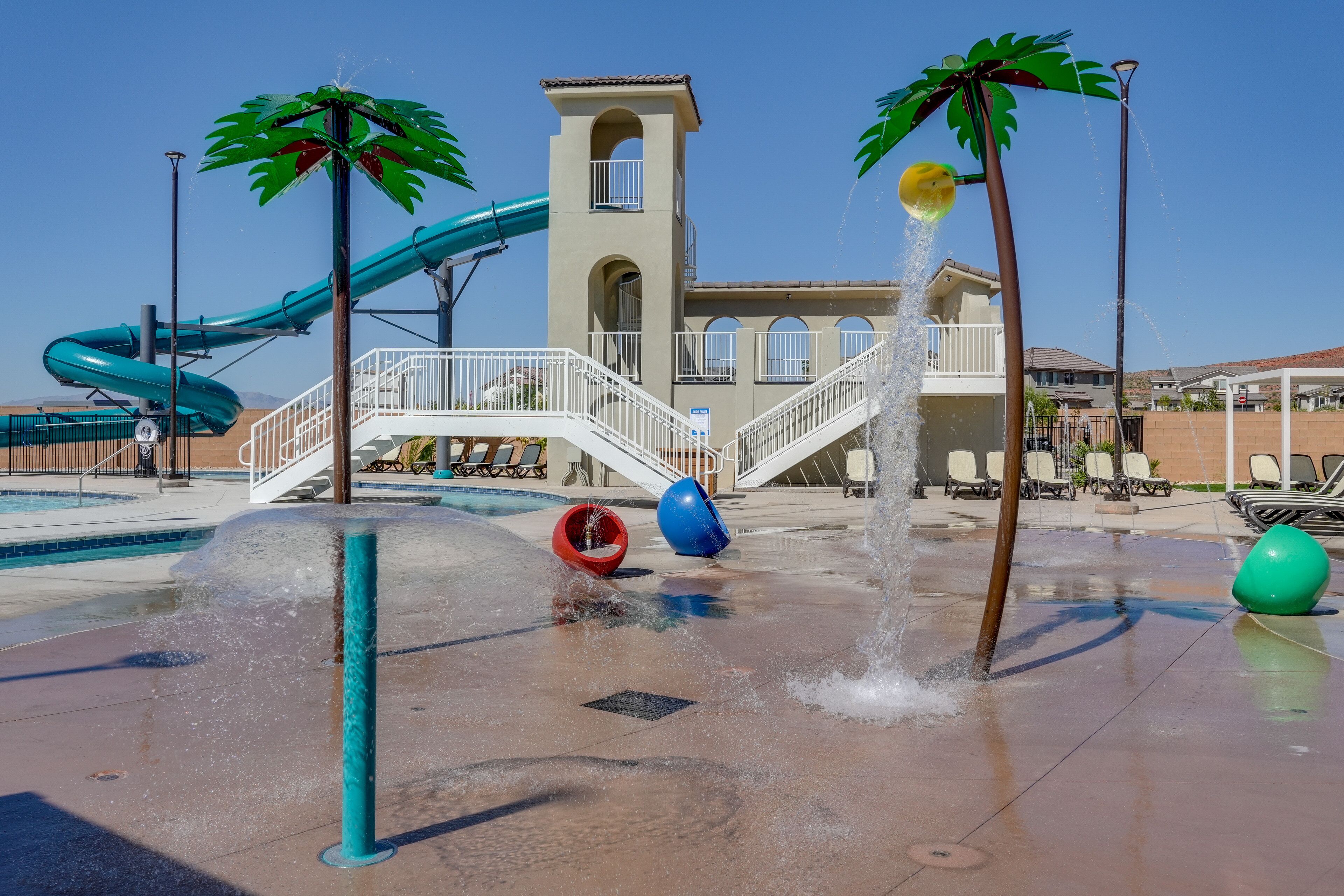 Un parc aquatique avec un toboggan, des jets d’eau et des palmiers.