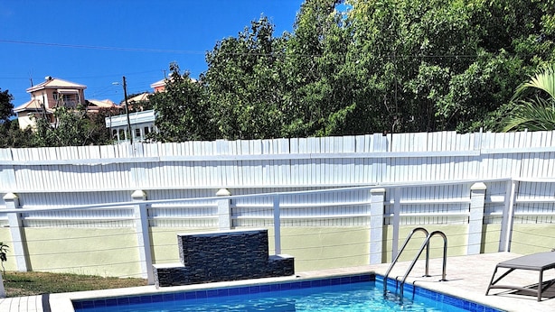 A rectangular swimming pool with clear blue water, surrounded by a white fence and a stone wall. There are two lounge chairs on the poolside. - The Cabin Retreat (Bonne Terre)