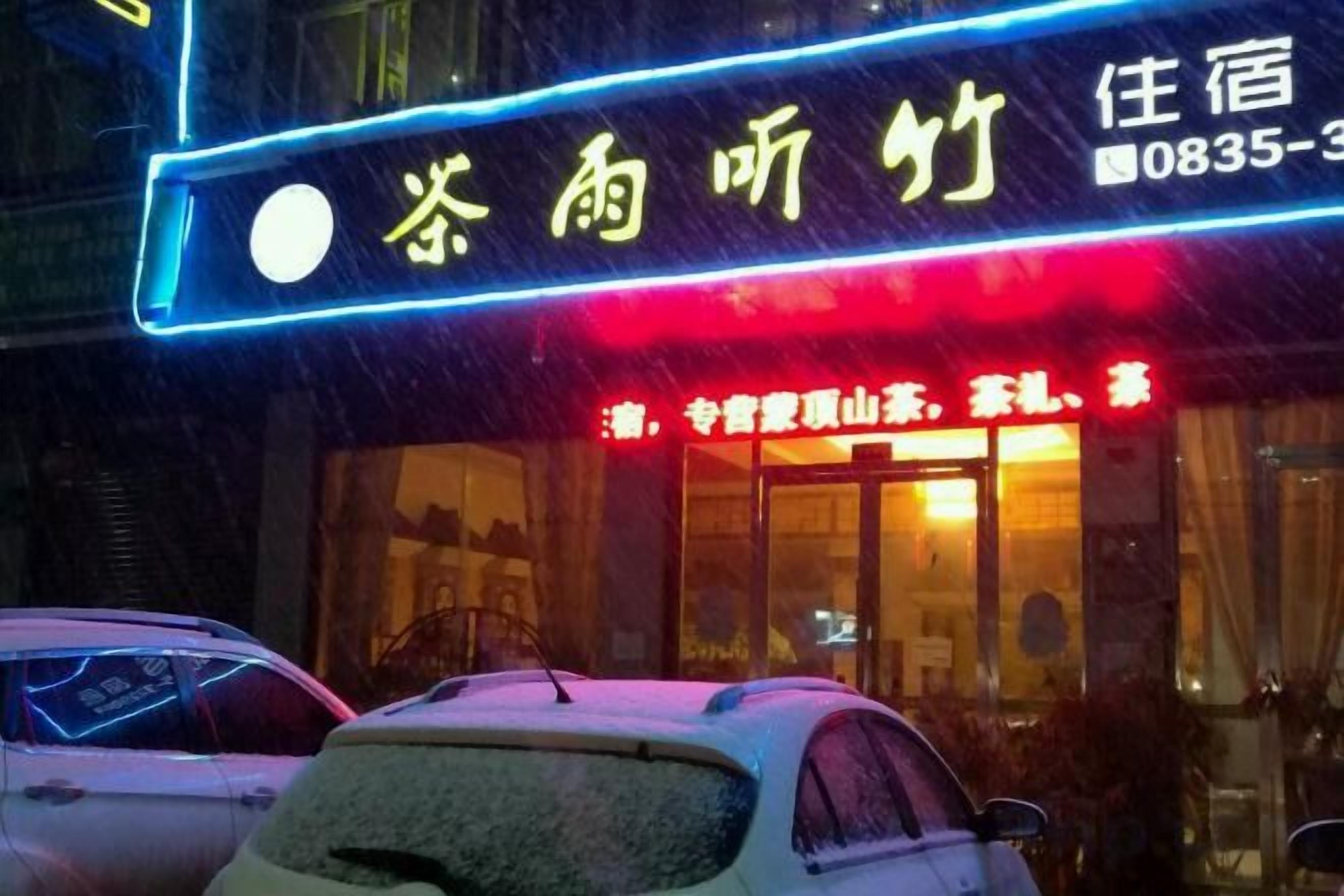 A hotel with a neon sign, a visible entrance, and a car parked in front.