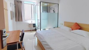 A modern hotel room with a bed, a desk, a chair, and a glass-enclosed shower area. - Chayu Tinzhu Hotel (Ya'an)