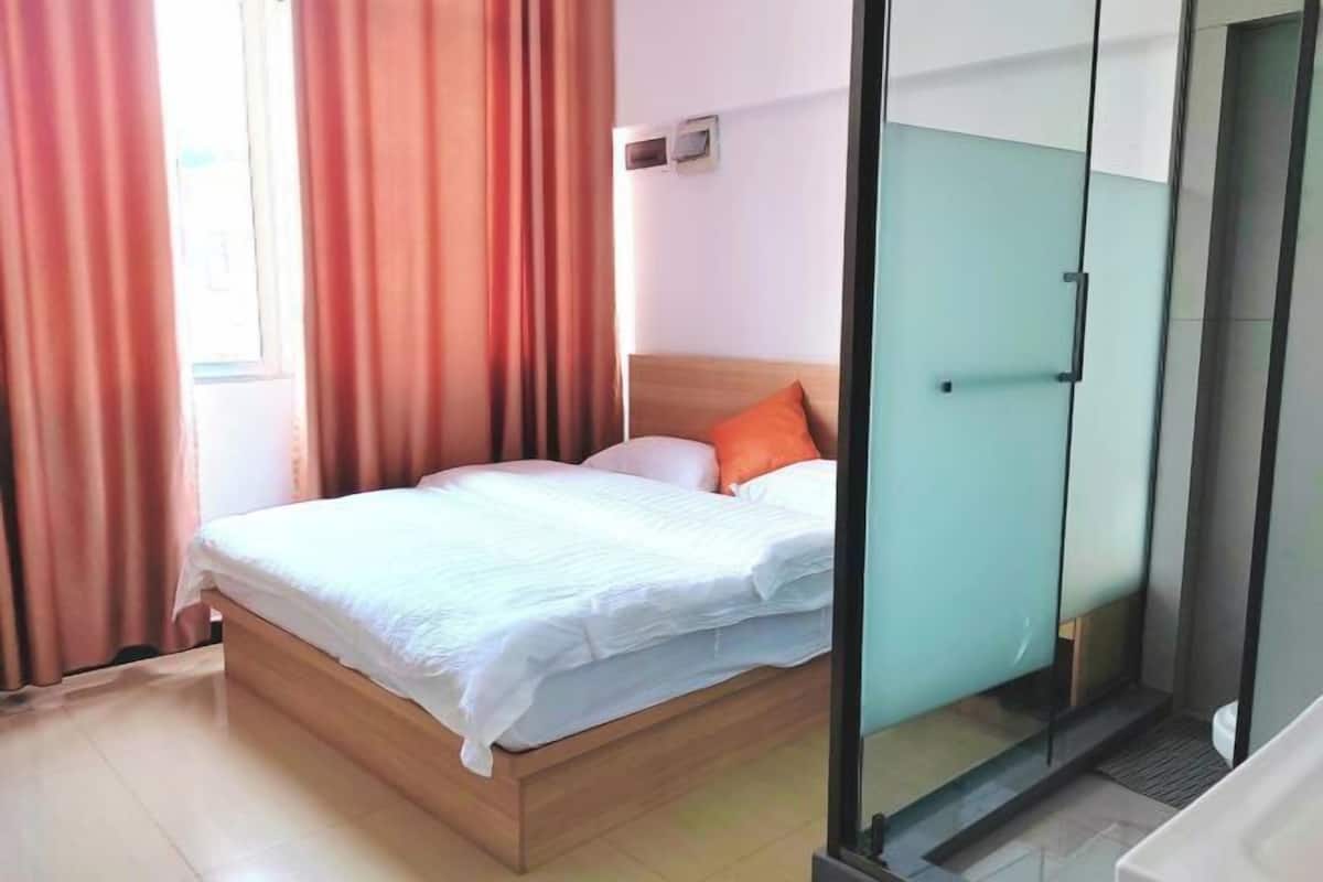 Un dormitorio con cama, cortinas, ventana y puerta de vidrio que da a un baño.