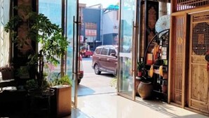 A hallway with a glass door leading outside, potted plants, and a wooden decorative panel on the right. - Chayu Tinzhu Hotel (Ya'an)