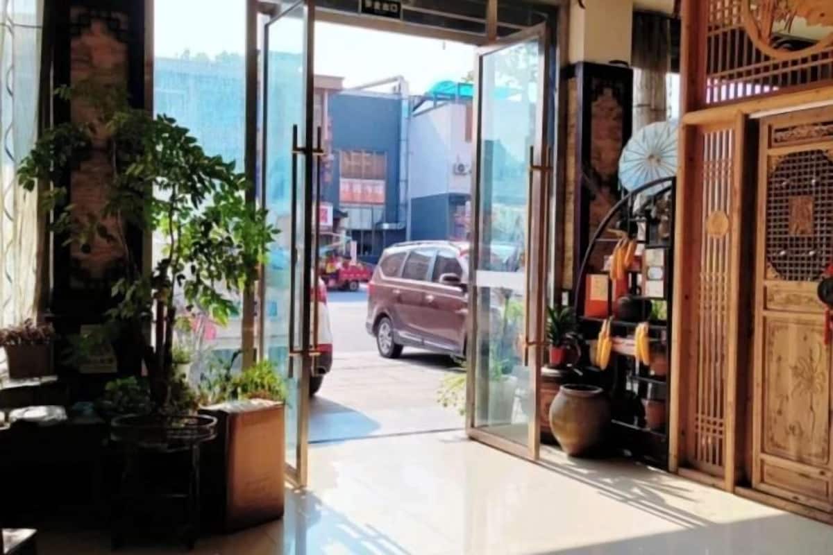 Un pasillo con puerta de cristal que da al exterior, plantas en macetas y un panel decorativo de madera a la derecha.