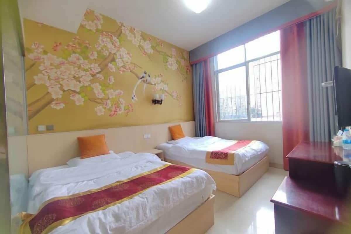 Habitación de hotel con dos camas, un ventanal grande, un mural en la pared y un escritorio con televisor.