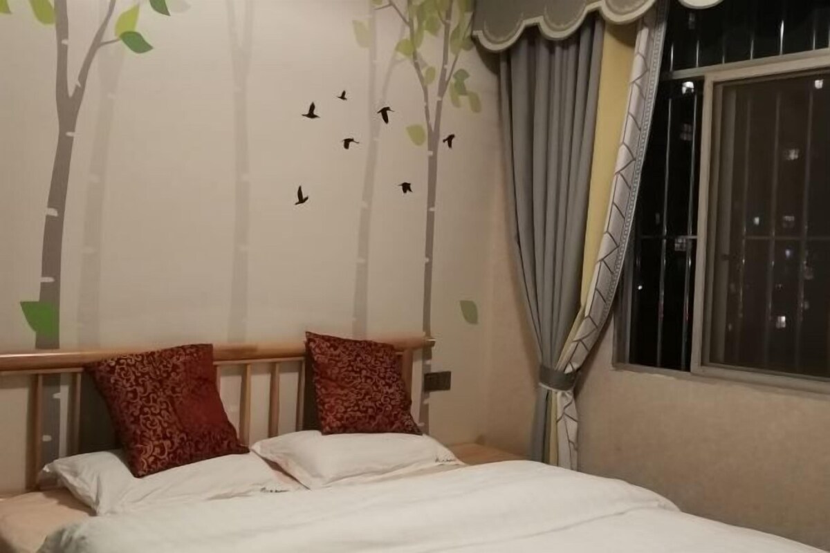 Una camera da letto con un letto, due cuscini, una parete decorata con un disegno di alberi e uccelli, una finestra con tende e un comodino.