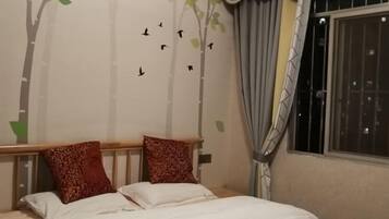 Ein Schlafzimmer mit einem Bett, zwei Kissen, einer Wand mit einem Wandbild von einem Baum und Vögeln, einem Fenster mit Vorhängen und einem Nachttisch.