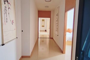 A hotel hallway with a polished floor, a door on the right, and a bed visible through an open door at the end.