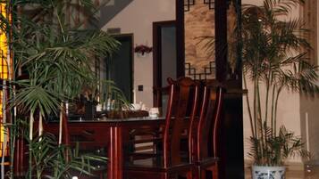A dining area with wooden chairs and a table, a potted plant, and a decorative wall.
