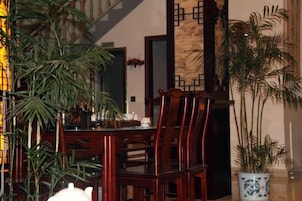 A dining area with wooden chairs and a table, a potted plant, and a decorative wall.