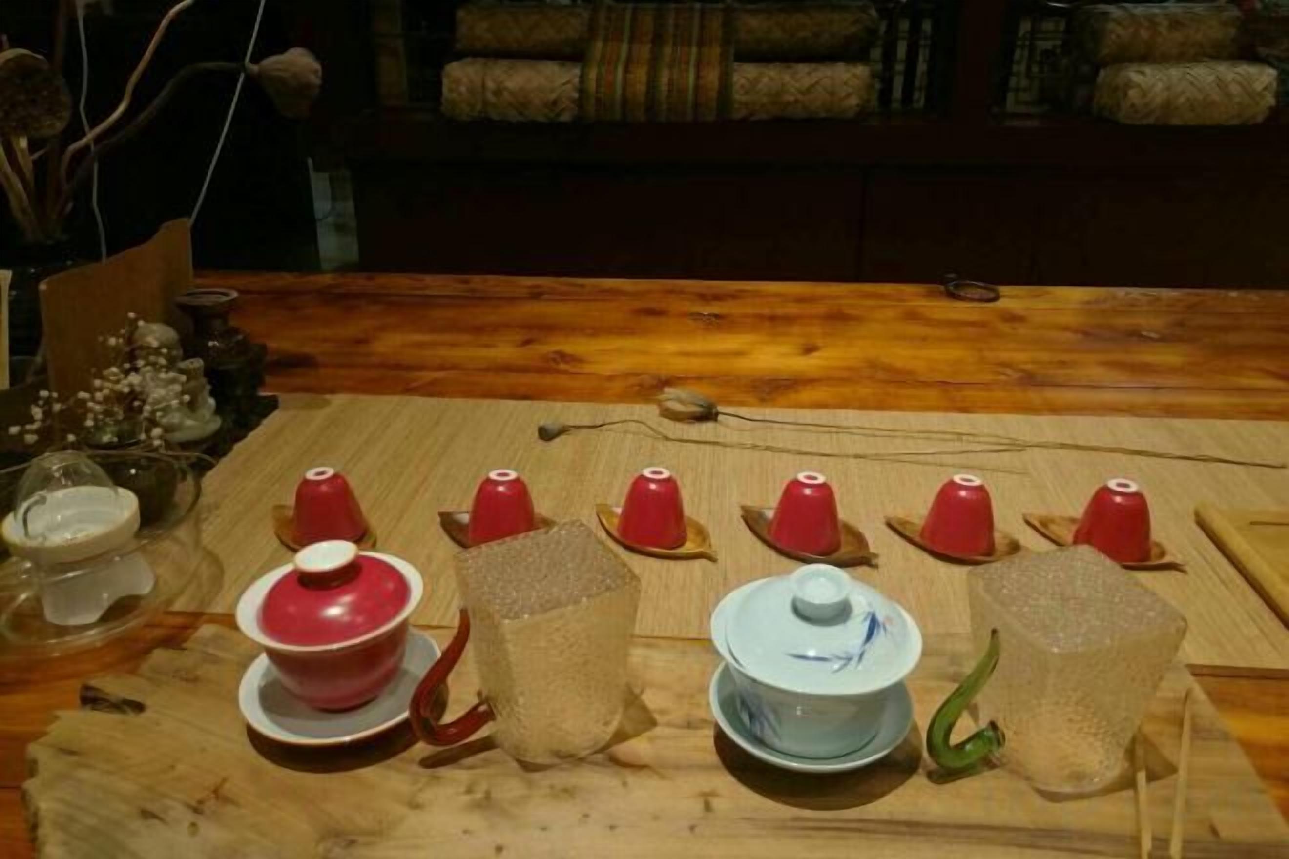 A wooden table with various ceramic cups and bowls, some with lids, and a small green object.
