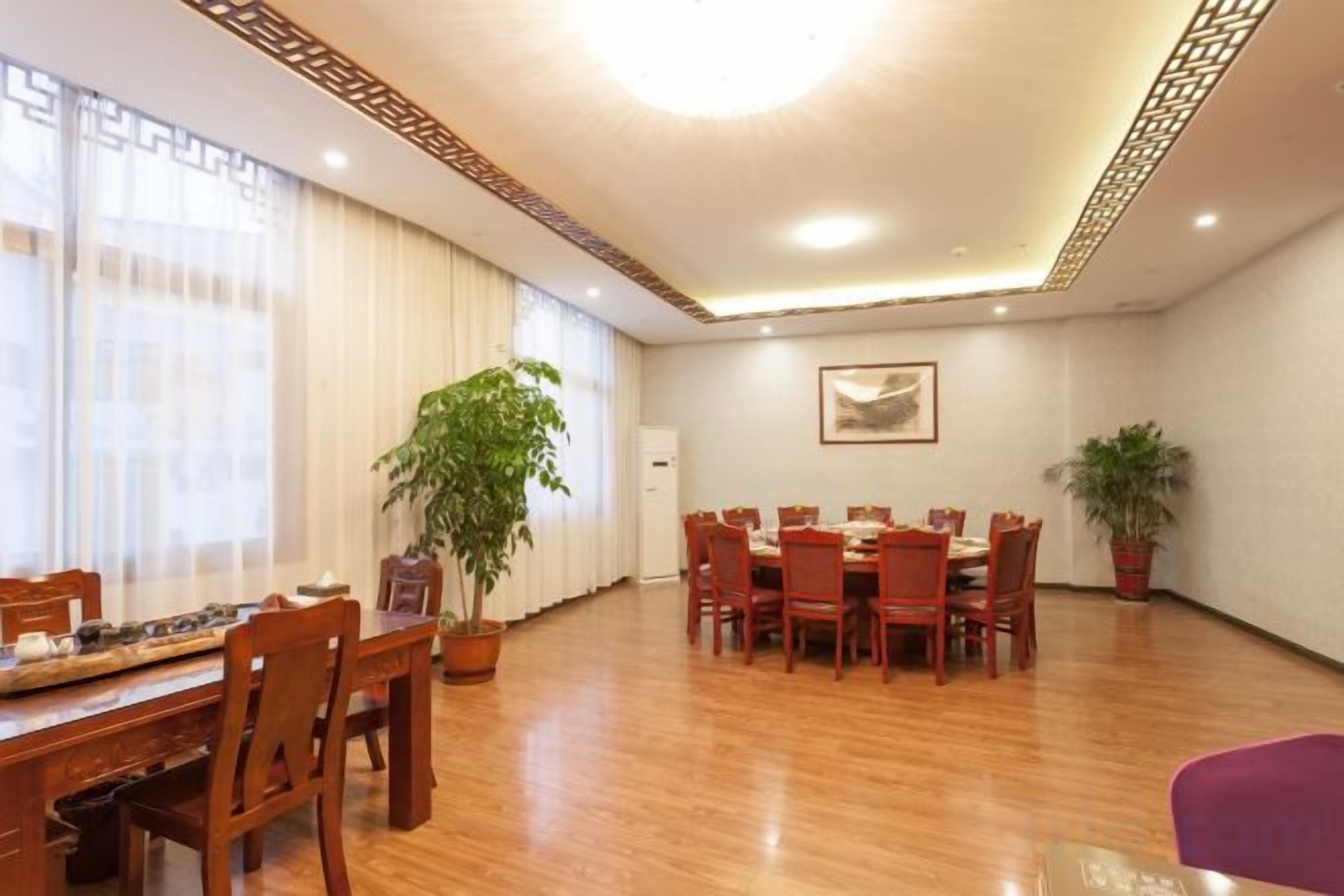 Un espace repas comprenant une longue table et des chaises, des plantes en pot et un plafond orné d’un motif décoratif.