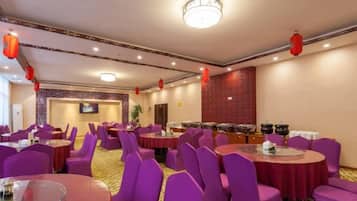 Un salón de banquetes con mesas redondas y sillas moradas, una zona de bufé y faroles rojos en el techo.