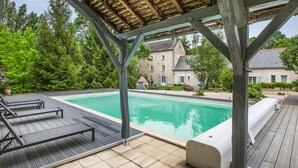A pool area with wooden deck, lounge chairs, and a covered seating area.