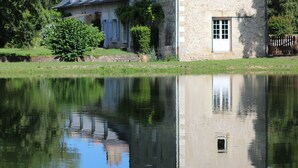 A stone building with a reflection in the water, surrounded by greenery.