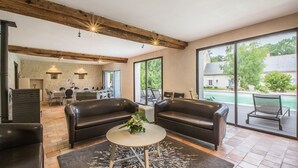 A spacious living area with leather sofas, a round coffee table, and a large glass door leading to a pool.