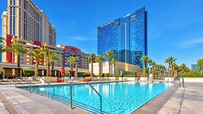 Un espace piscine d’hôtel avec une piscine à l’eau cristalline, des chaises longues et des palmiers.