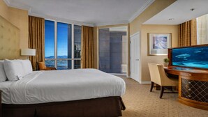 Ein Hotelzimmer mit einem großen Bett, einem Schreibtisch mit Fernseher und Blick auf die Stadt durch große Fenster.
