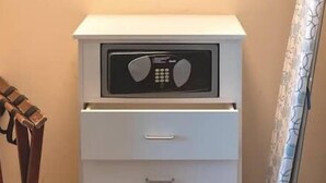 Ein kleiner, weißer Nachttisch mit Radio und Schublade in einem Schlafzimmer mit Bett und Vorhang.