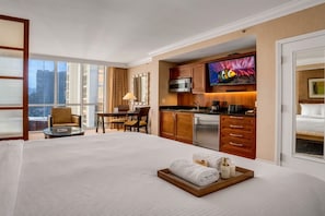 Quarto de hotel com cama grande, área de refeições, cozinha compacta e televisão.