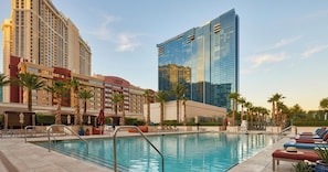 A hotel pool area with a clear view of the hotel's architecture, including a modern glass building and a classic hotel facade.