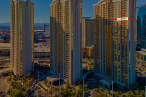 A high-rise building with multiple floors, surrounded by other tall buildings and a parking area with several cars.