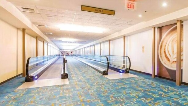 Un pasillo largo y vacío, con una escalera mecánica en el centro que conduce a un piso superior.