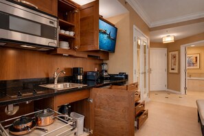 A modern kitchen with stainless steel appliances, wooden cabinetry, and a flat-screen TV mounted above the counter.