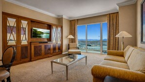 Habitación de hotel con un ventanal grande que ofrece vistas a la ciudad, un televisor de pantalla plana, un sofá, una silla y una mesa de centro.