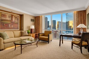 Una habitación de hotel con un ventanal grande, un sofá, una silla, una mesita y una lámpara.