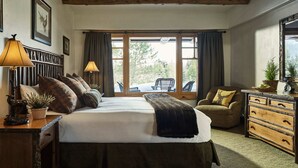 Un dormitorio con una cama grande, dos lámparas de noche, un aparador, una silla y una ventana con vistas a árboles.
