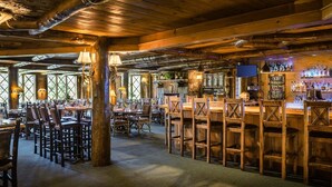 Un interior rústico de madera con mesas y sillas, una zona de bar con botellas y una chimenea de piedra.