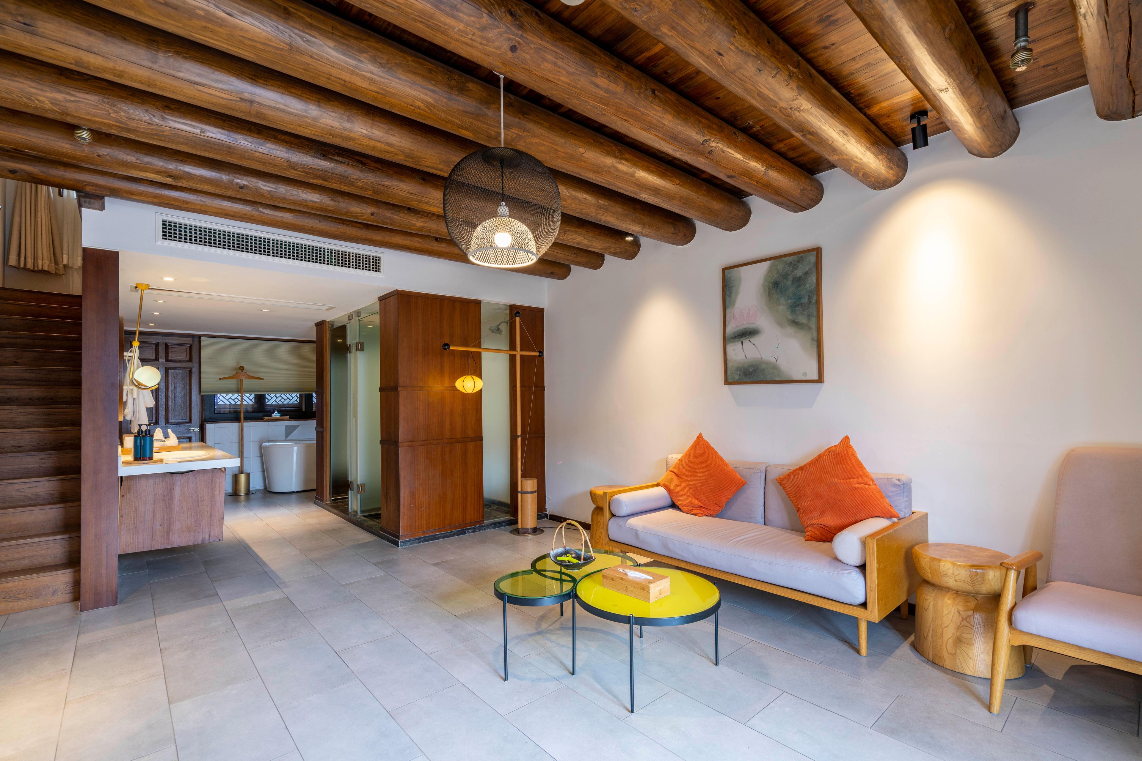 A modern living room with a wooden ceiling, a sofa with orange cushions, a small wooden side table, and a round coffee table.