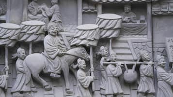 A detailed stone carving of a historical scene with figures, including a seated individual on a horse and others carrying drums and a basket.