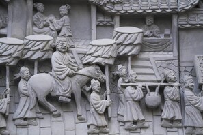 Un detallado relieve de piedra que representa una escena histórica con figuras, incluyendo una persona sentada sobre un caballo y otras llevando tambores y una cesta.