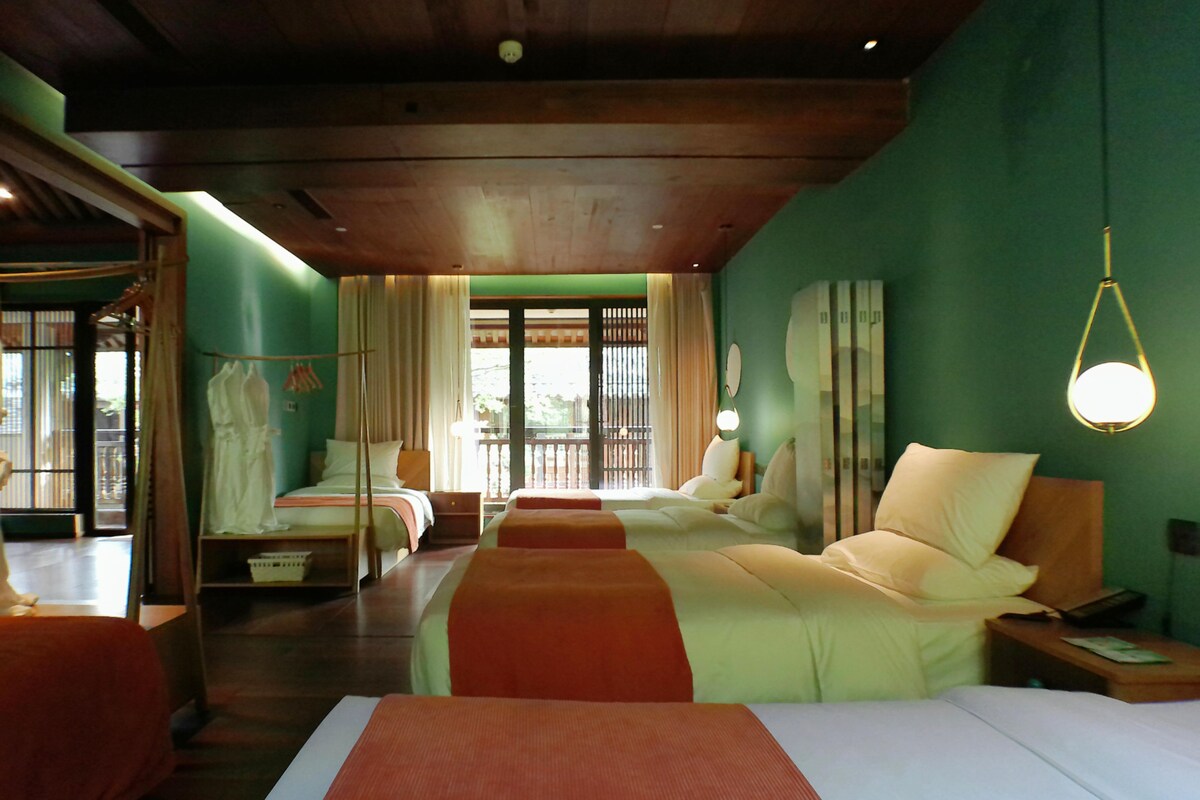 A hotel room with two beds, a nightstand, a lamp, and a view of the outdoors.