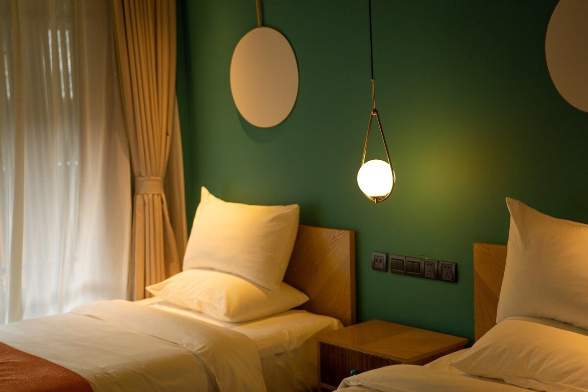 A hotel room with two beds, a hanging light fixture, and a green wall.