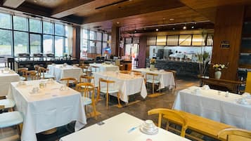 A restaurant with multiple tables and chairs, a kitchen area, and large windows allowing natural light.
