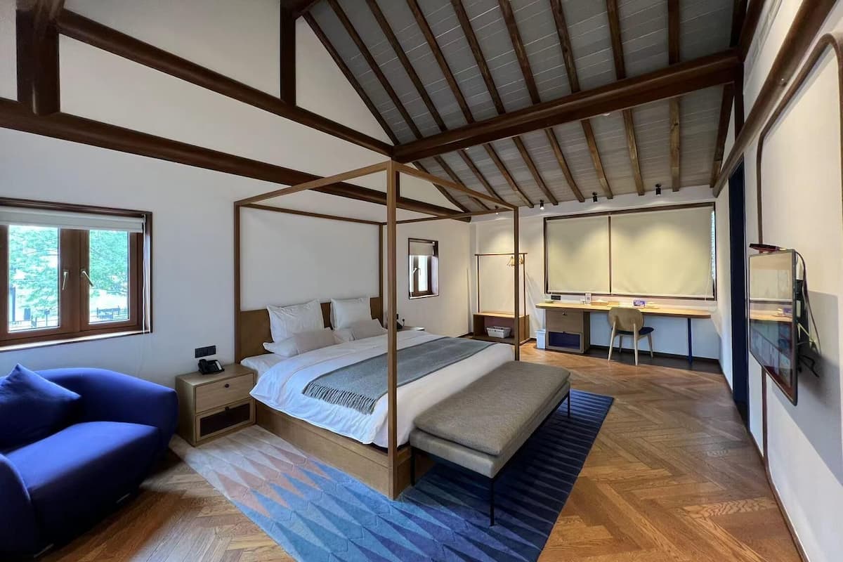 A bedroom with a four-poster bed, a desk, a chair, and a sofa.