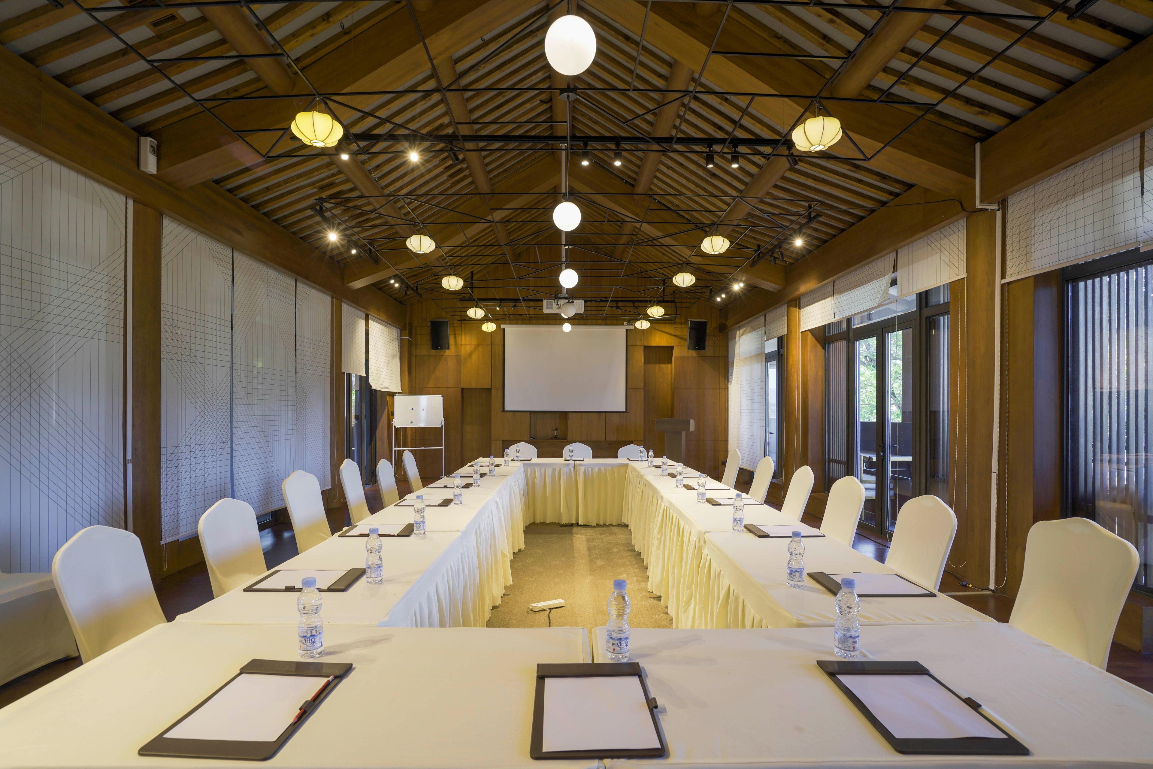 A conference room with a long table, white chairs, water bottles, and a projector screen.