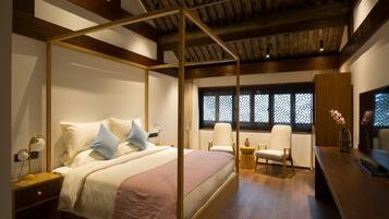 A bedroom with a four-poster bed, bedside tables, a desk, chairs, and a window with patterned shutters.
