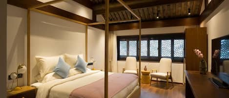 A bedroom with a four-poster bed, bedside tables, a desk, chairs, and a window with patterned shutters.