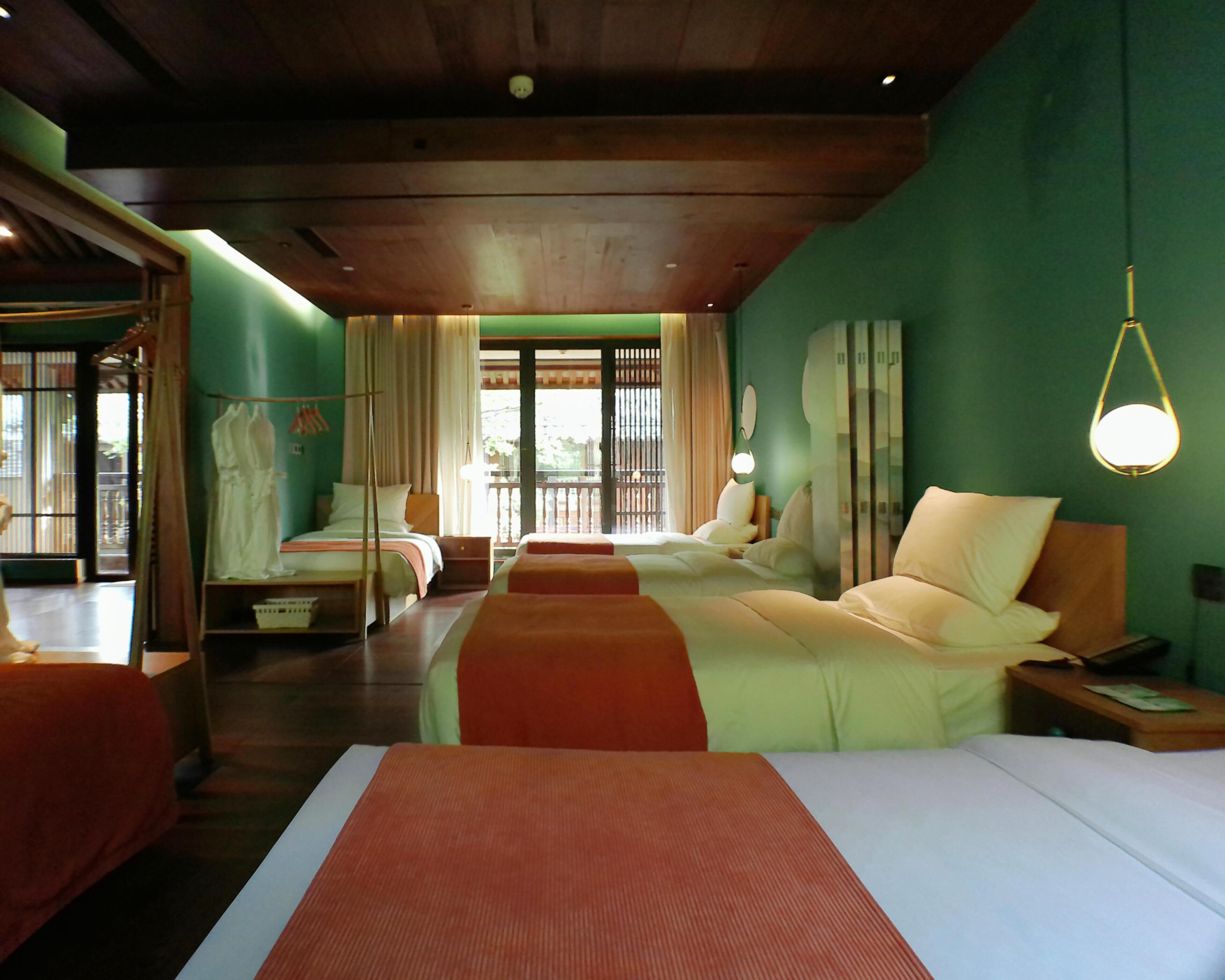 A hotel room with two beds, a nightstand, a lamp, and a view of the outdoors.
