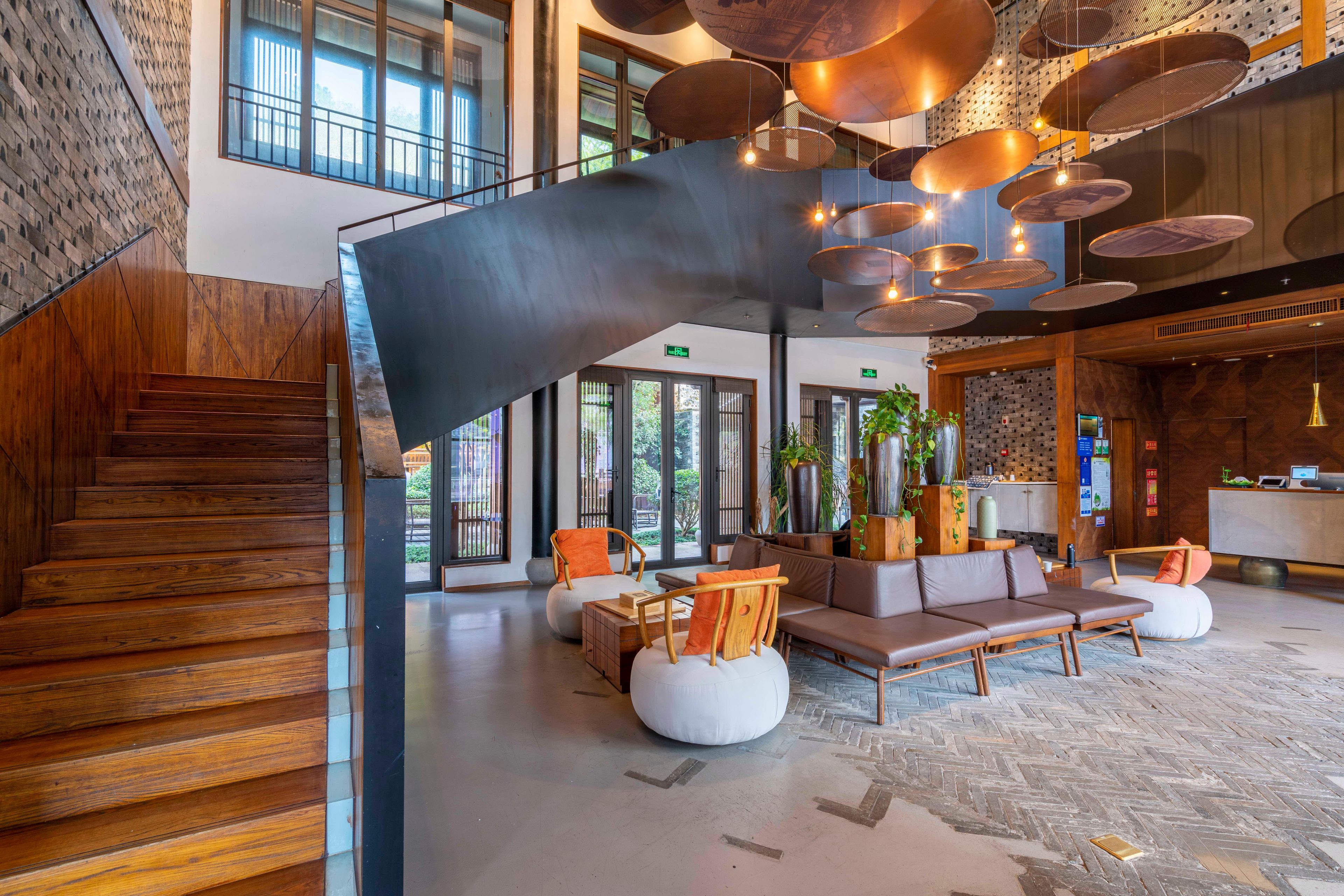 Eine moderne Lobby mit einer Holztreppe, Sitzbereichen und einer großen Hängeleuchte.