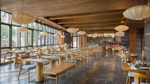 A spacious restaurant with wooden tables and chairs, large windows, and hanging pendant lights. - Blossom Hill Hotel Ningbo Hanling (Ningbo)