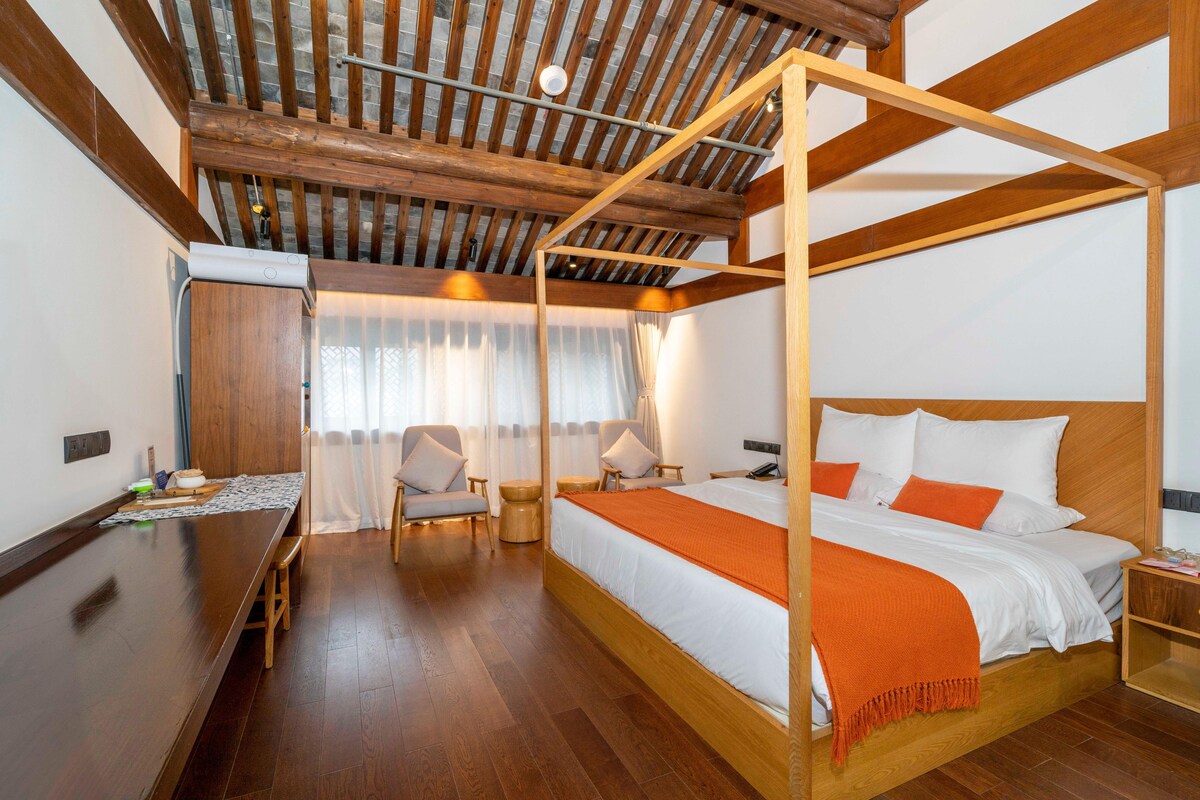 Quarto com cama de dossel, piso de madeira, mesa de jantar e área de estar com cadeiras.